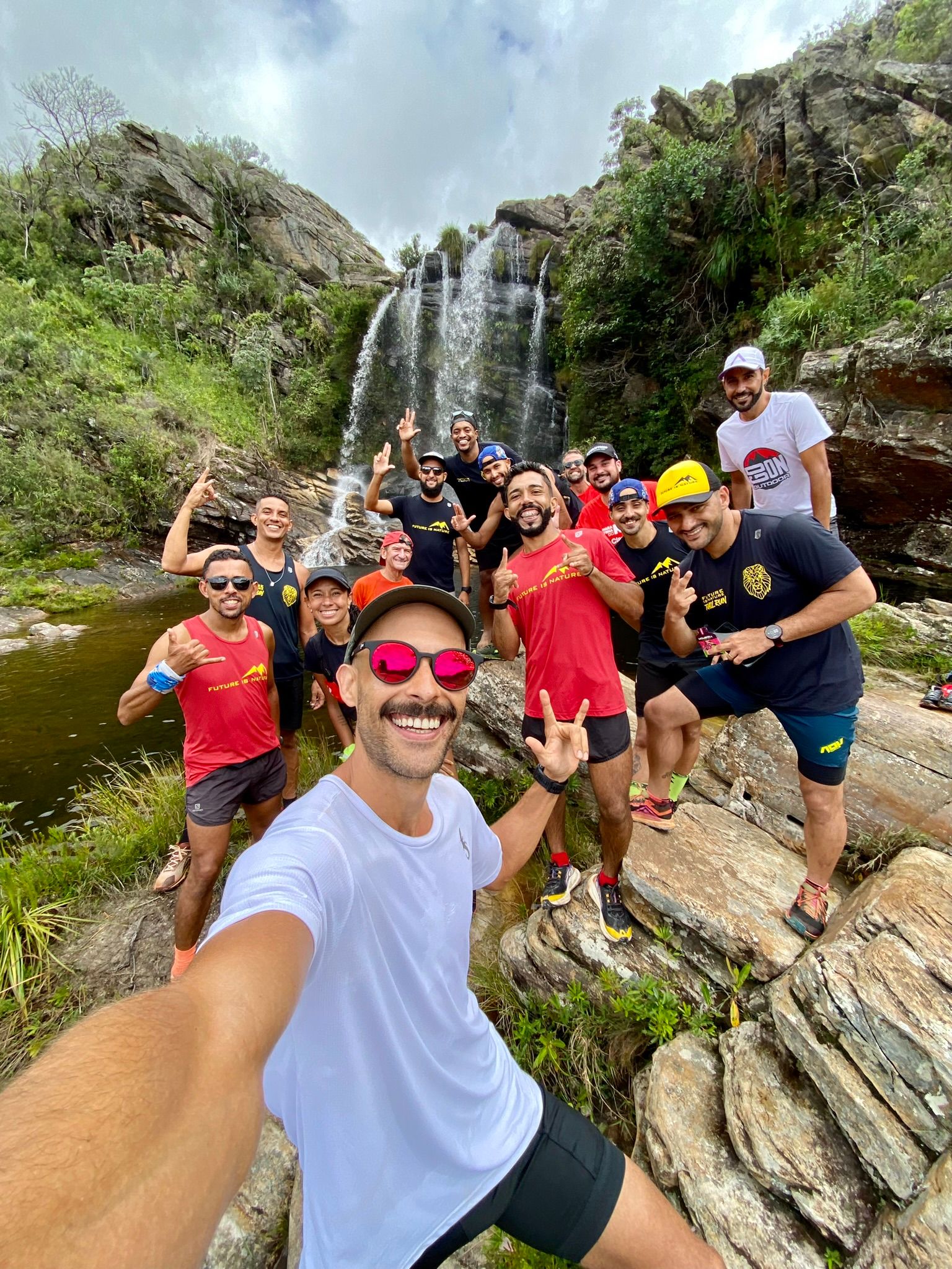 Grupo de corredores reunido na pedra ao pé de uma cachoeira, sorrindo para a foto depois do treino