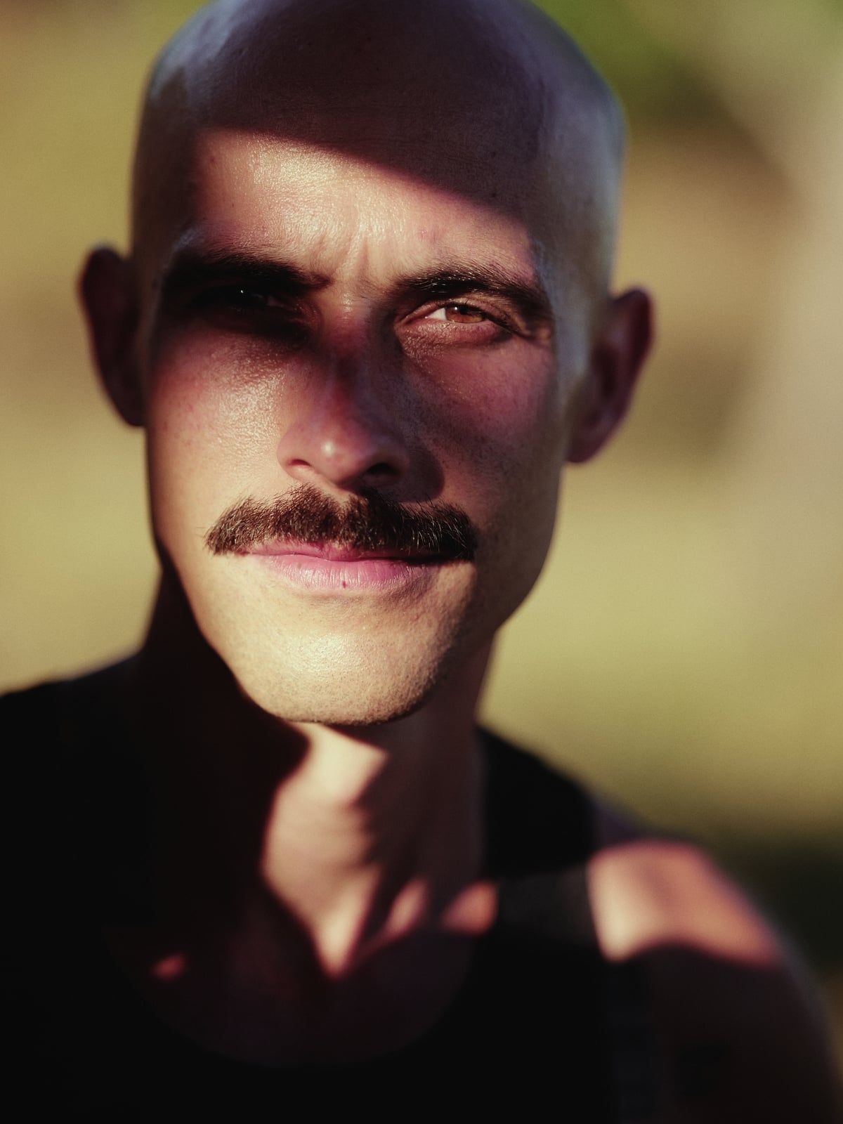 Retrato de Diogo França ao ar livre, olhando para a câmera com o rosto meio iluminado pelo sol