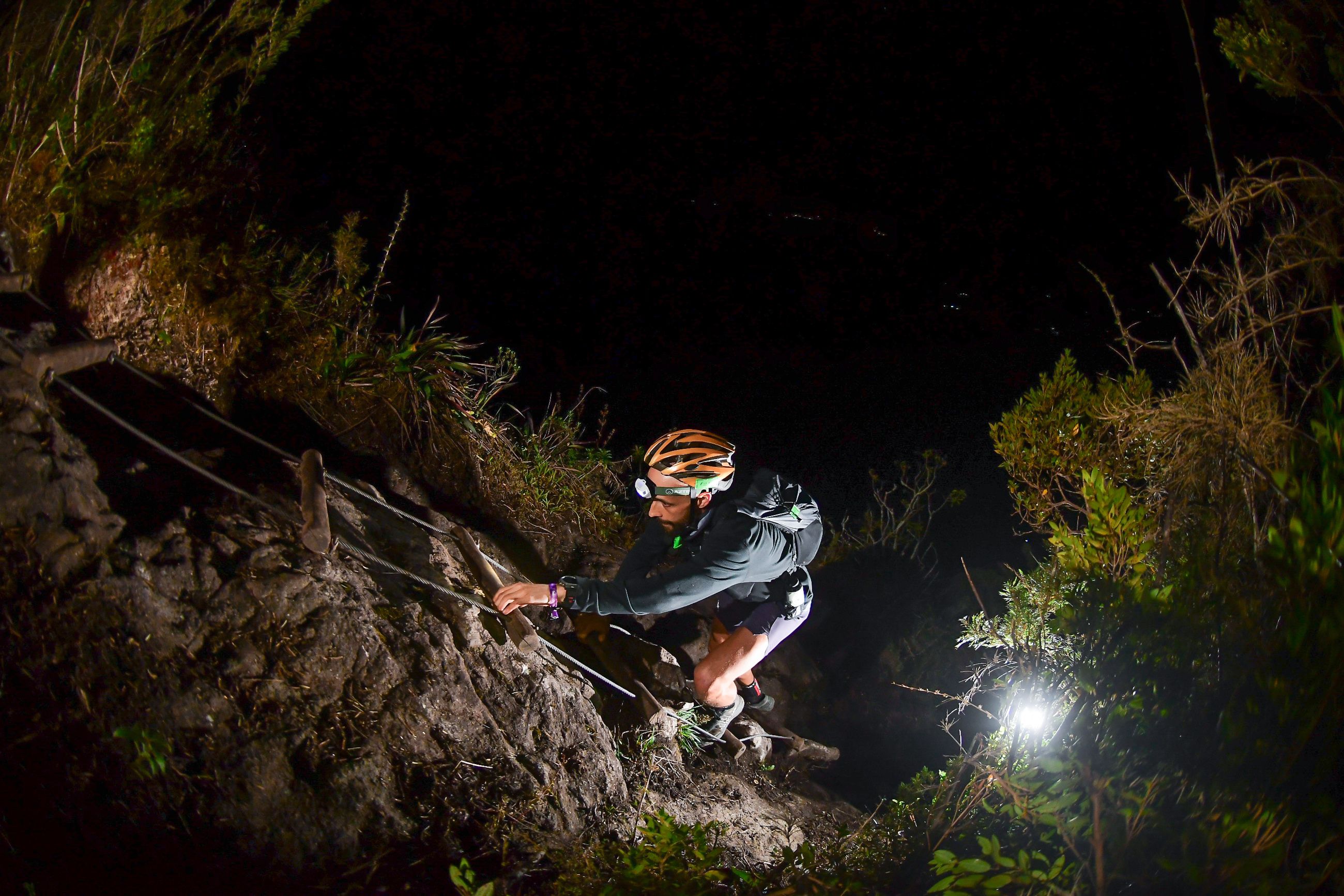 Corredor de lanterna de cabeça agarrado a um cabo de aço em rocha molhada durante a noite